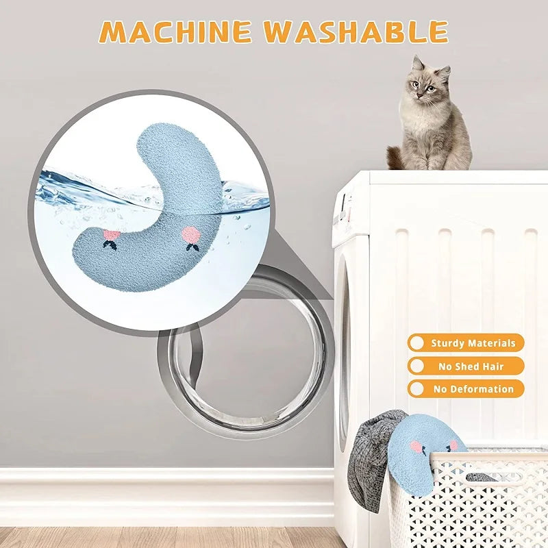 The cat pillow going into a washing machine, with a cat sitting on top of the machine